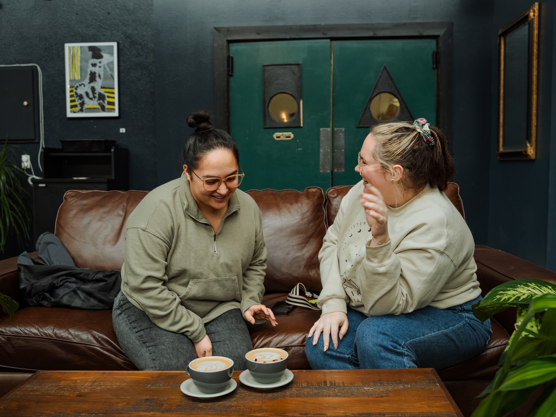 Two guests enjoying lattes on the leather couch at Earth Coffeehouse